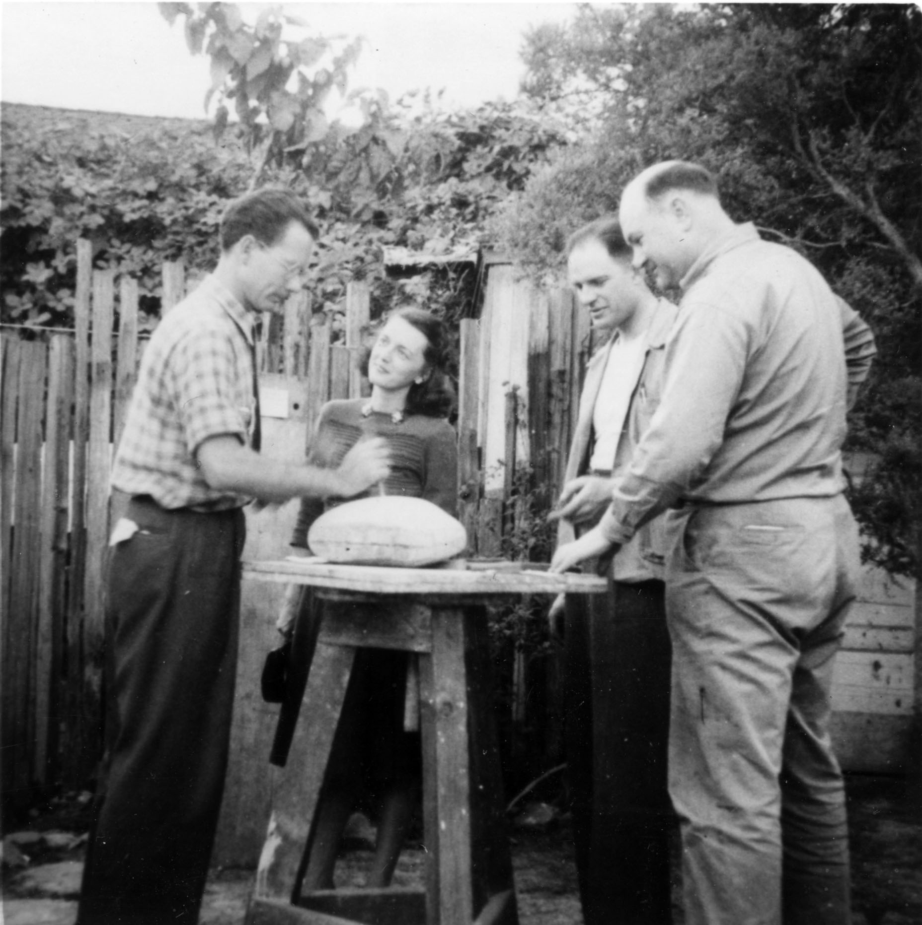 Several men and women standing around a sculpture work table in process.